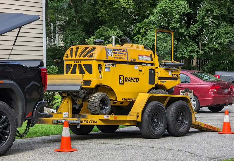 Tow-behind stump grinder parked on a residential street with safety cones